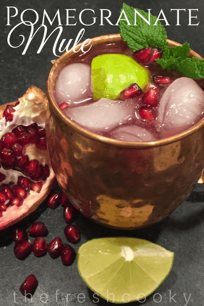 Pomegranate Mule in copper mug with ice and pomegranate arils on top with a fresh twist of lime and mint.