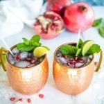 Two copper cups filled with pomegranate moscow mule.