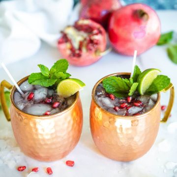 Two copper cups filled with pomegranate moscow mule.