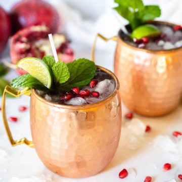 Two copper cups filled with festive holiday cockatils, pomegranate moscow mule.