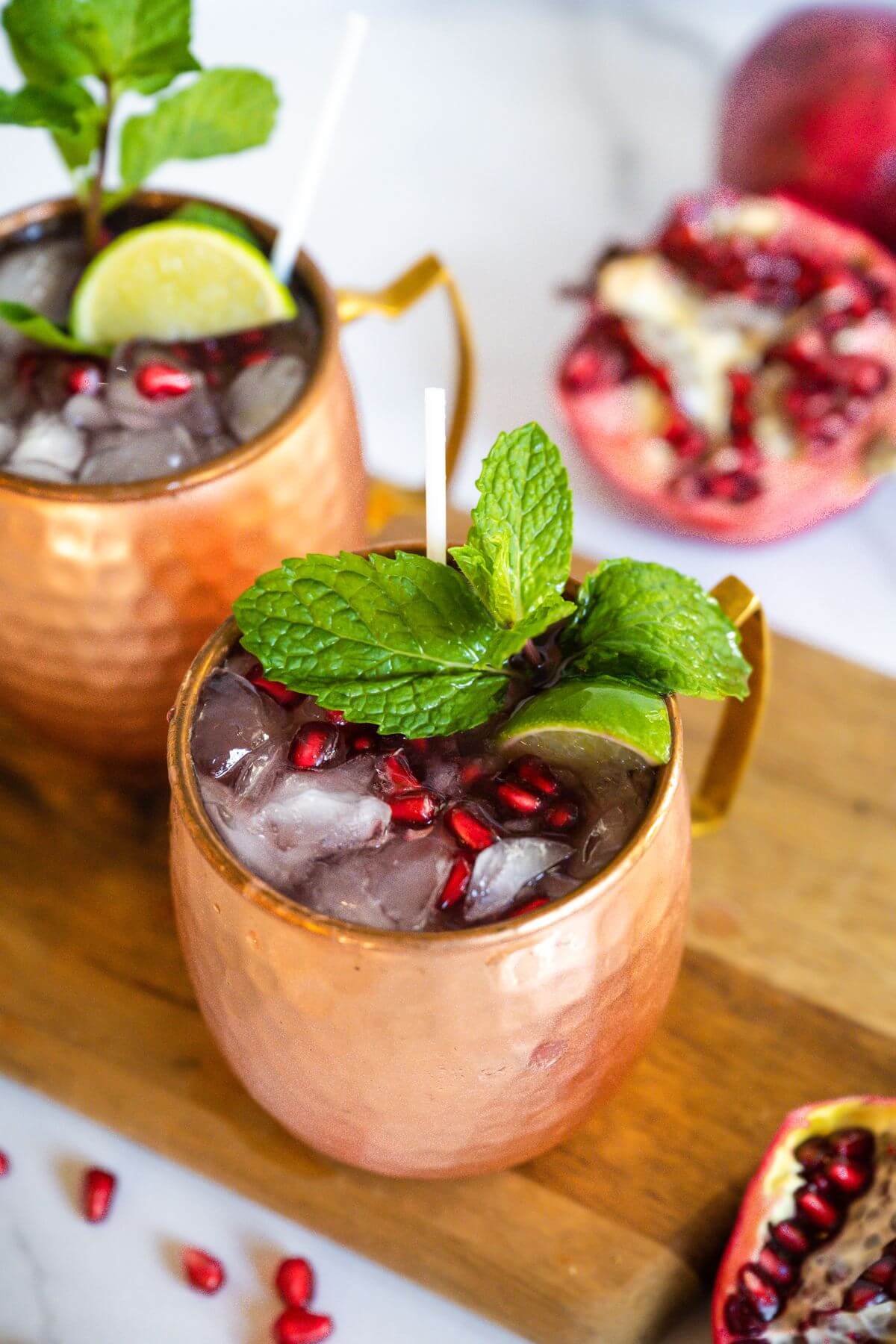 Holiday mule garnished with mint, limes, and pomegranate arils, in two copper mugs.