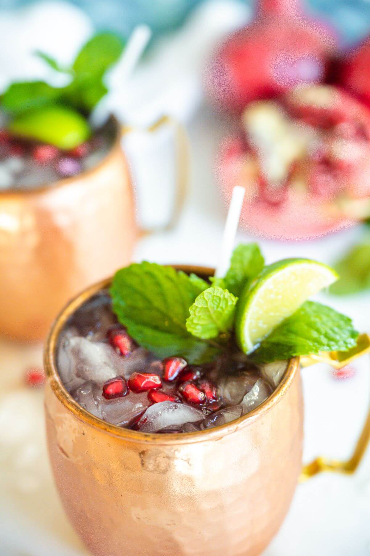 A holiday yule mule in a copper mug, garnished with a mint sprig, lime and pomegranate arils.