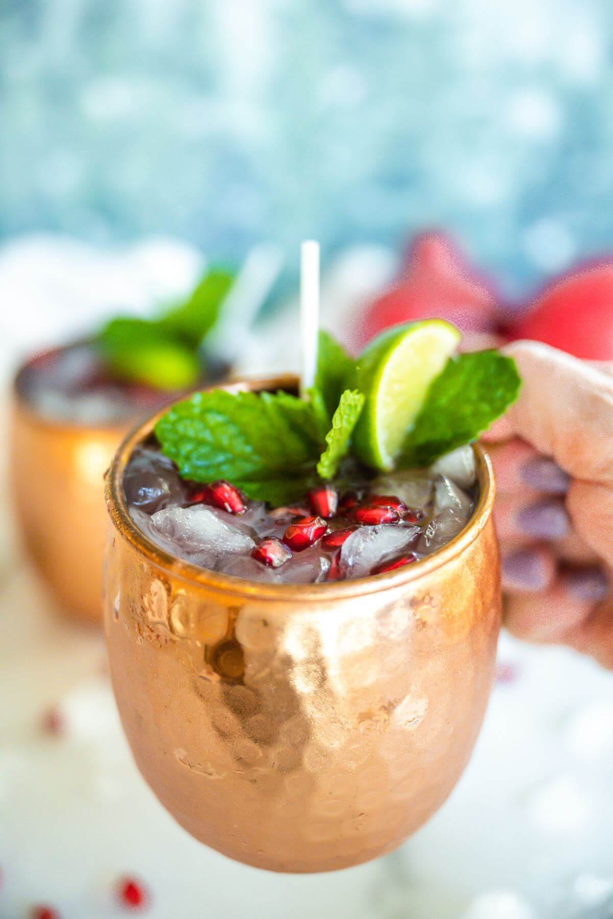 Hand holding copper mug filled with pomegranate mule.