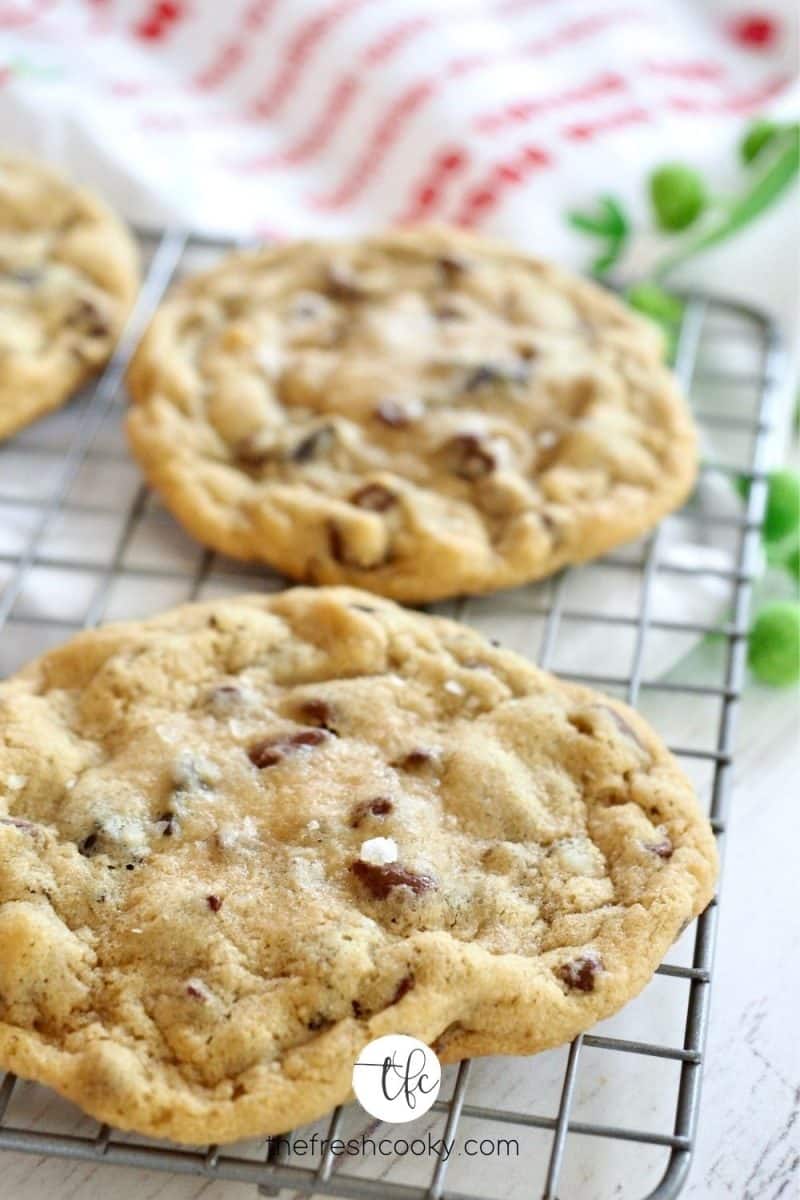 Two chocolate chip cookies on wire rack with tea towel in background.