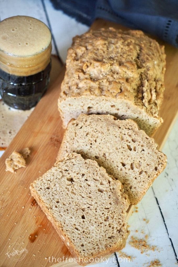 Top down shot of beer bread sliced on a cutting board with an overflowing glass of dark beer on the side. 