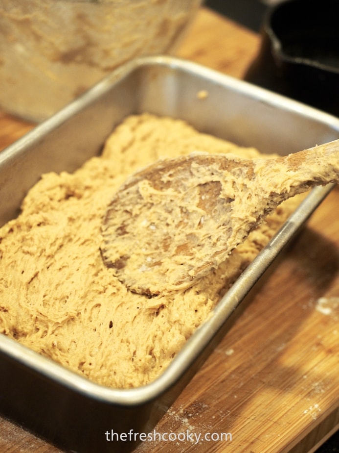 Using a wooden spoon to smooth the top of beer bread batter into a loaf pan. 