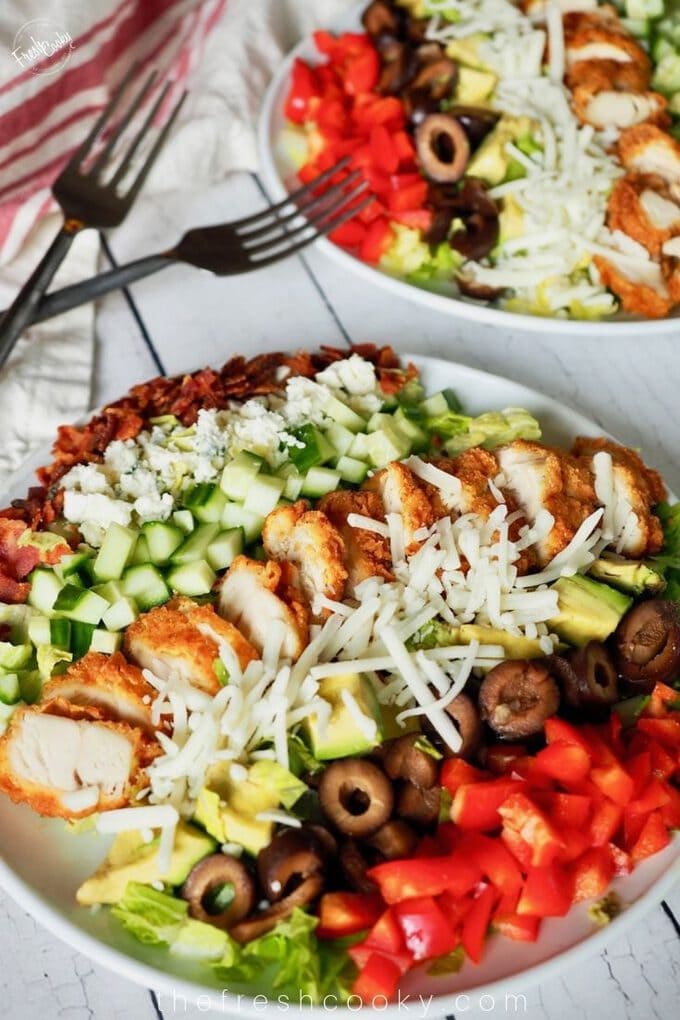 Plate of chicken cobb salad on white wood background with chicken tenders sliced on top. 