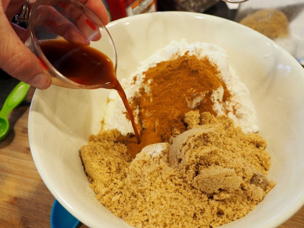 A bowl filled with brown sugar, butter, cinnamon and flour while pouring in vanilla for coffee cake crumb topping.