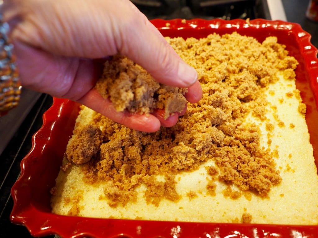 Hand placing rich buttery crumb topping on top of hot coffee cake.