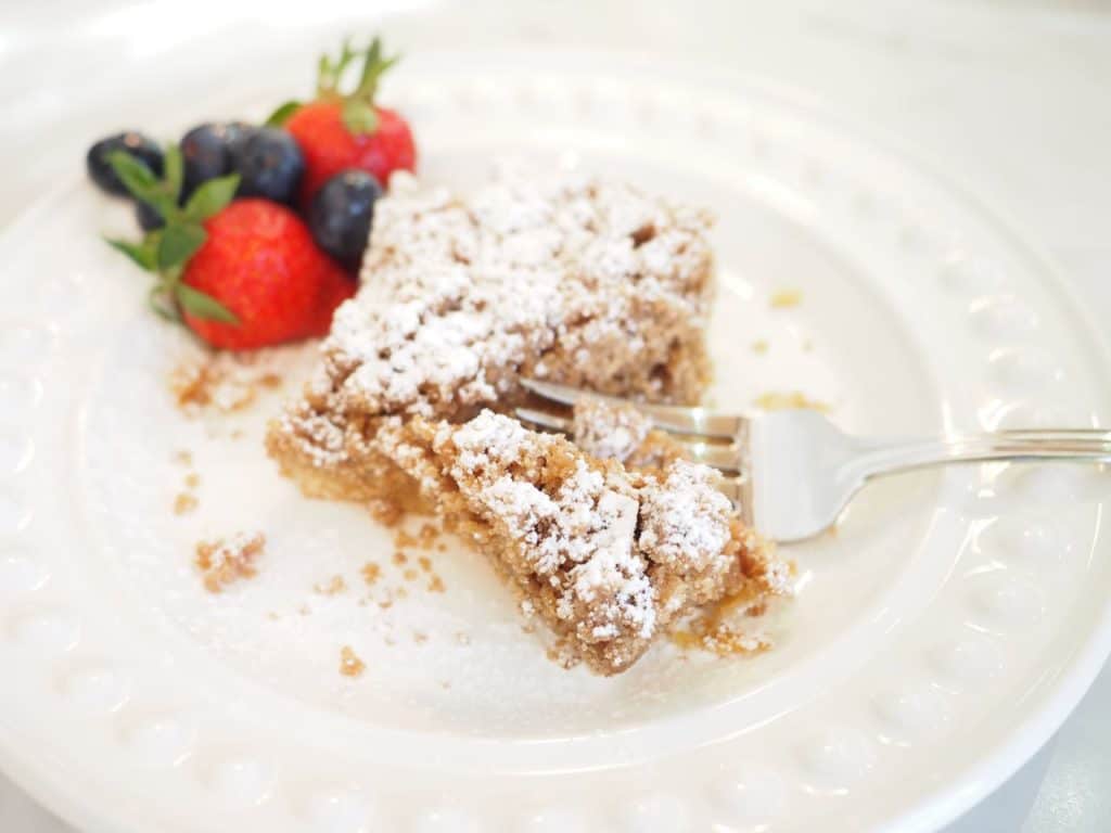 Square of Starbucks Coffee Crumb Cake on white plate with fork pie and a few berries. 