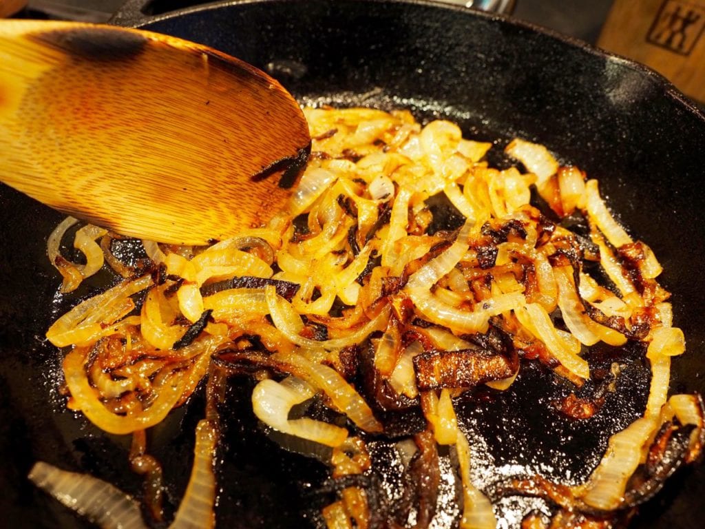 cast iron pan with wooden spoon grilling or caramelizing onions for burgers. thefreshcooky.com 
