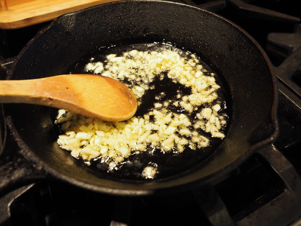 minced garlic simmering and toasting in a cast iron pan with wooden spoon. 