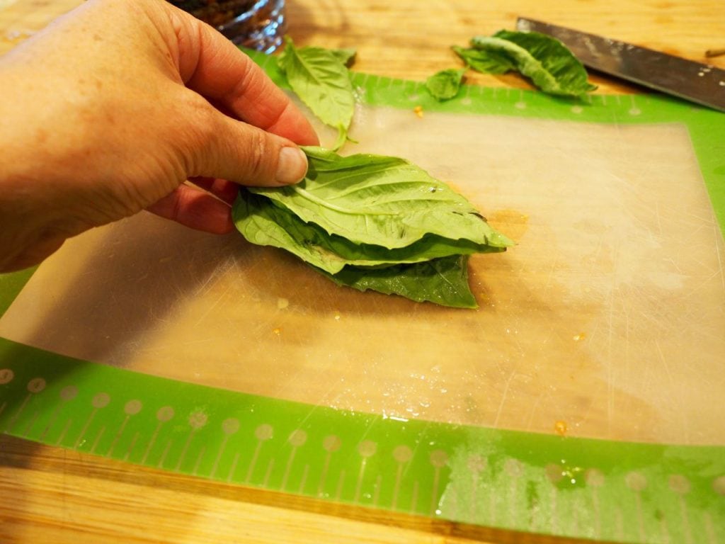 basil leaves stacked on cutting board, hand holding ends. 