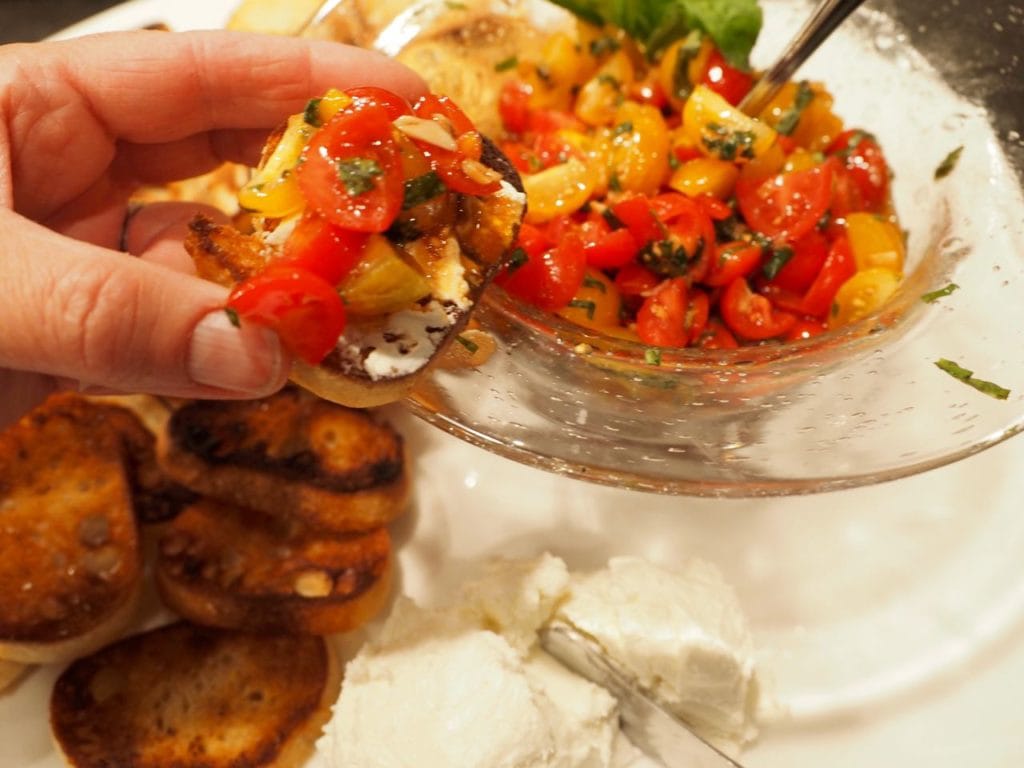 hand holding crostini smeared with goat cheese and topped with bruschetta mixture. 