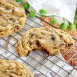 Chunky chocolate chip cookies high altitude on cooling rack one broken in half with a a bite.