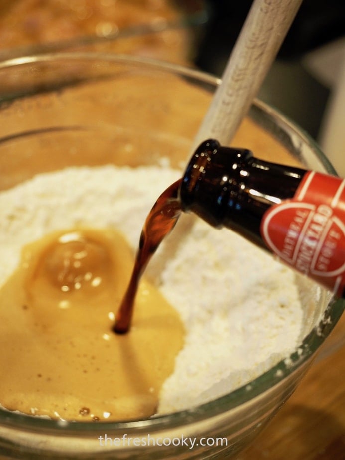 Pouring beer into beer bread ingredients in glass mixing bowl.