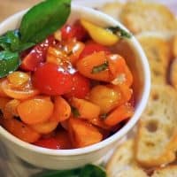 Easy and AMAZING Tomato Bruschetta is the perfect appetizer for any occasion. Warm garlic olive oil poured over fresh cut grape tomatoes, fresh basil and drizzled with balsamic vinegar. Spread a little creamy goat cheese on the crostini then top with bruschetta. #thefreshcooky #bruschetta #tomatoes #appetizer #easy