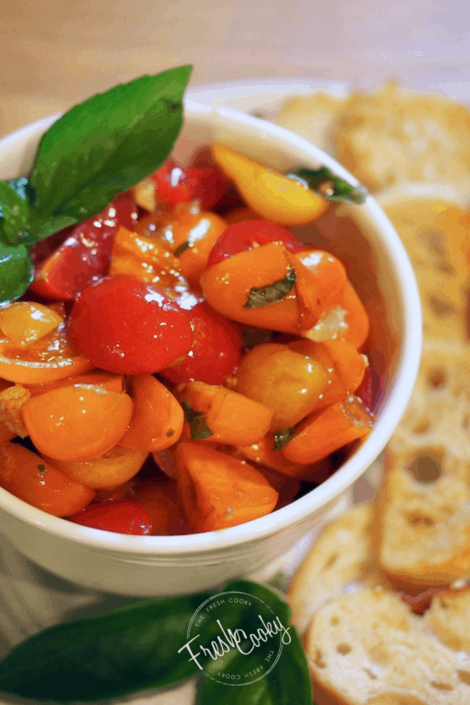 Pinterest image of white bowl with grape tomato bruschetta with leaves of basil, and french bread baguette slices