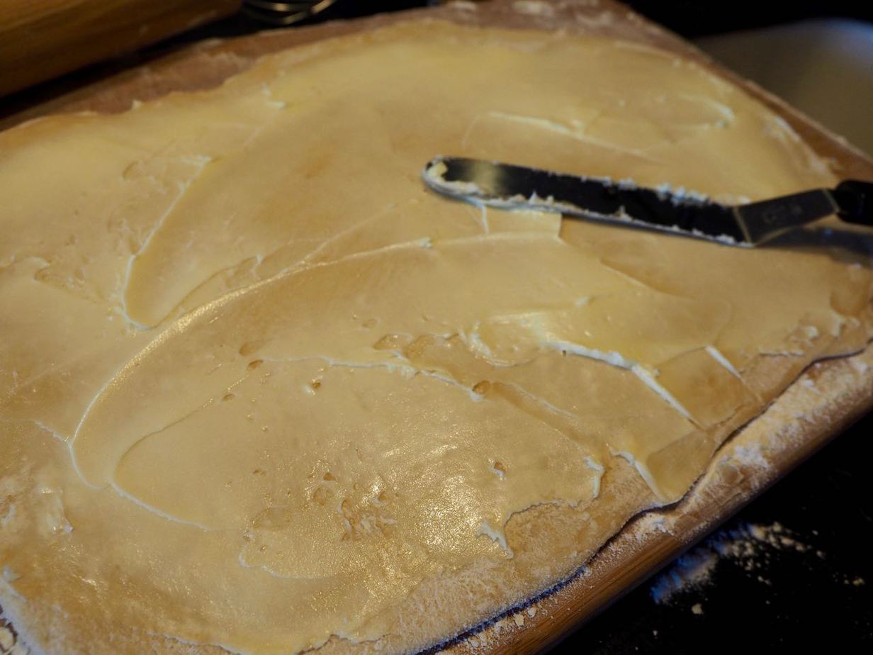 Spreading soft butter onto cinnamon roll dough with offset spatula.