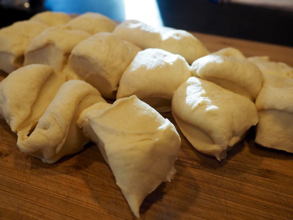 Yeast roll dough divided into 16 equal pieces on a bread board. 