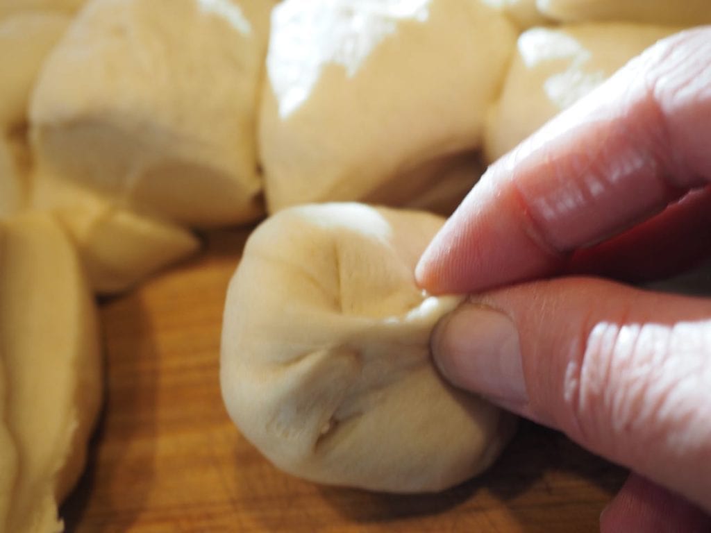 Hands pinching the individual bread dough pieces into little round dumplings. 