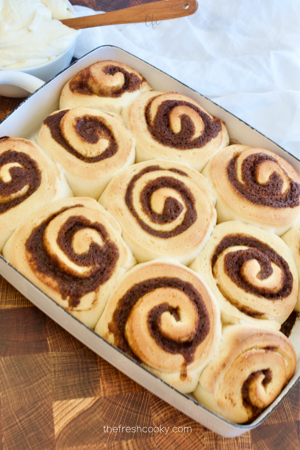 Pan of baked cinnamon rolls hot out of the oven with frosting nearby.