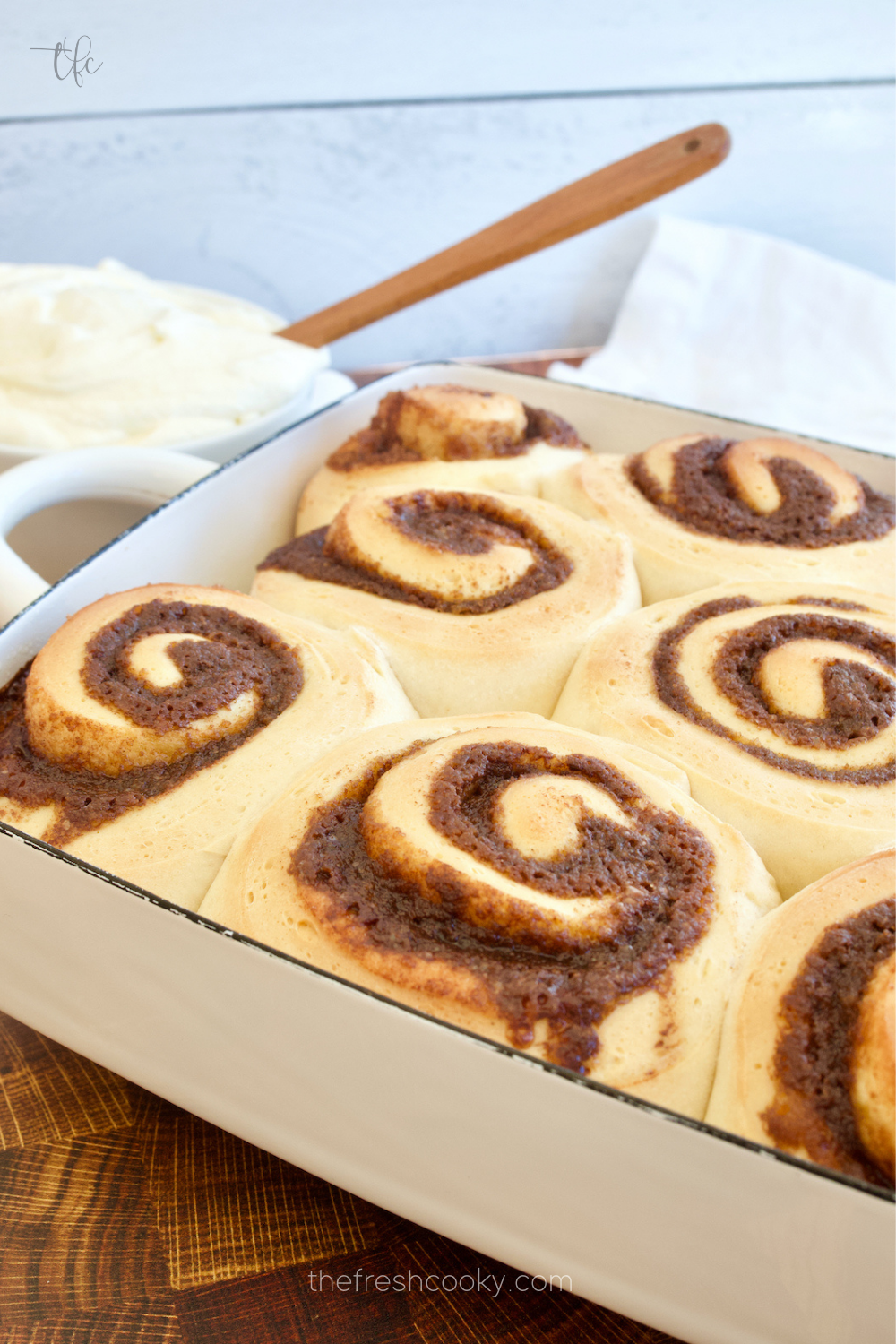 Pan of hot, soft cinnamon rolls with bowl of cream cheese frosting ready to be frosted.