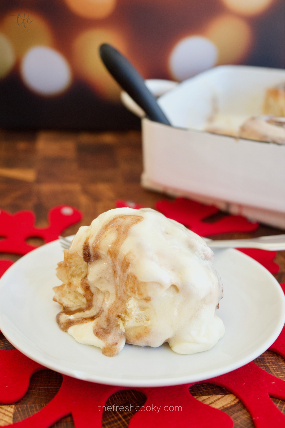 Holiday Cinnabon Clone cinnamon bun on a plate with sparkly lights behind.