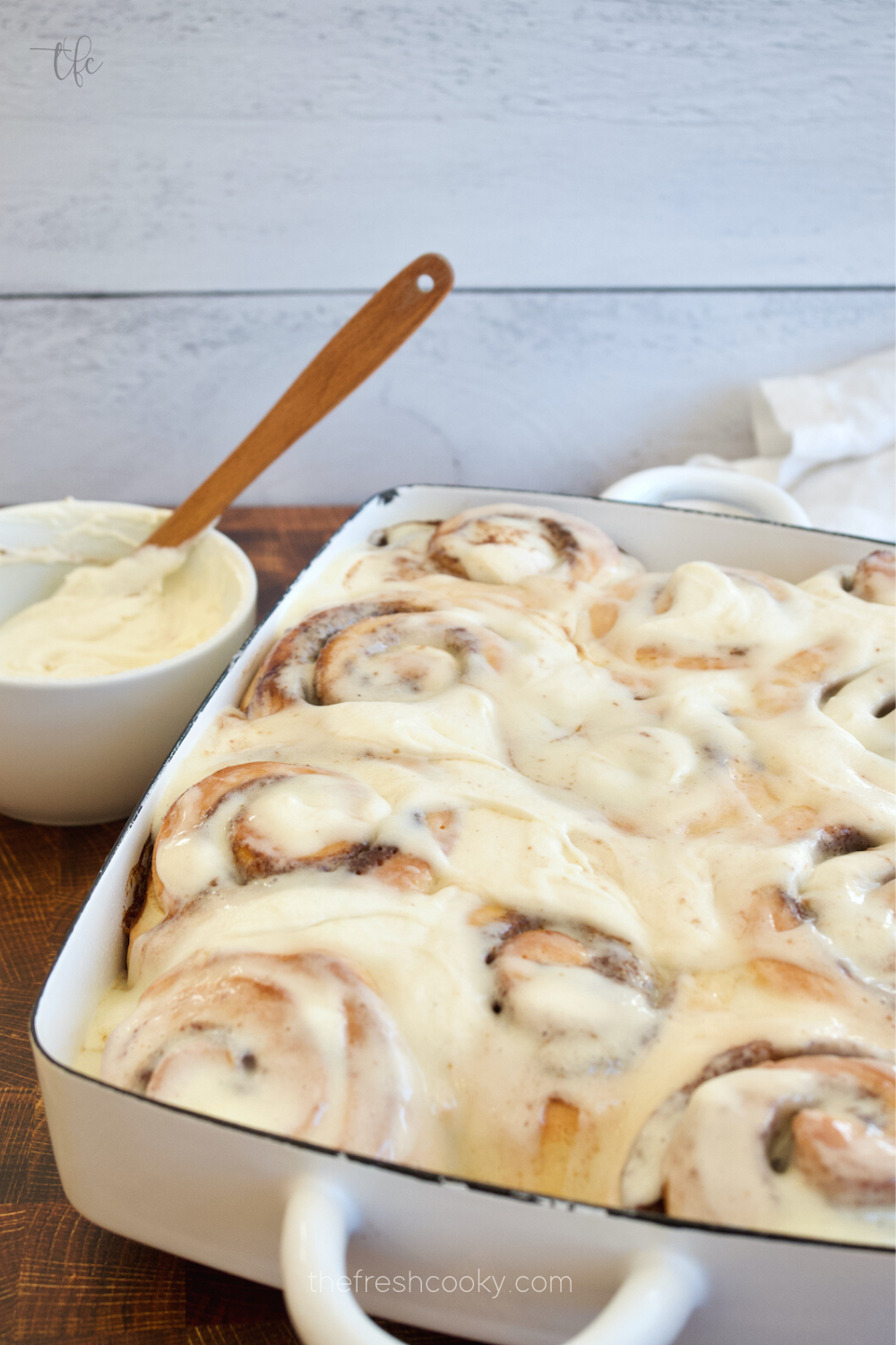 Pan filled with soft, fluffy gooey cinnamon rolls with bowl of frosting close by.