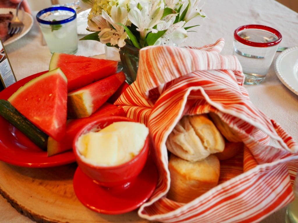 Summer table set with flowers, wedges of fresh watermelon, hot biscuits and butter in a crock. | www.thefreshcooky.com