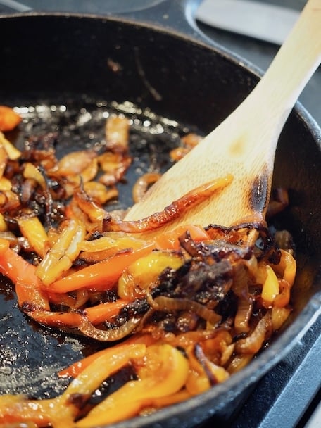 Cast iron pan with caramelized onions and peppers and a wooden spoon | www.thefreshcooky.com