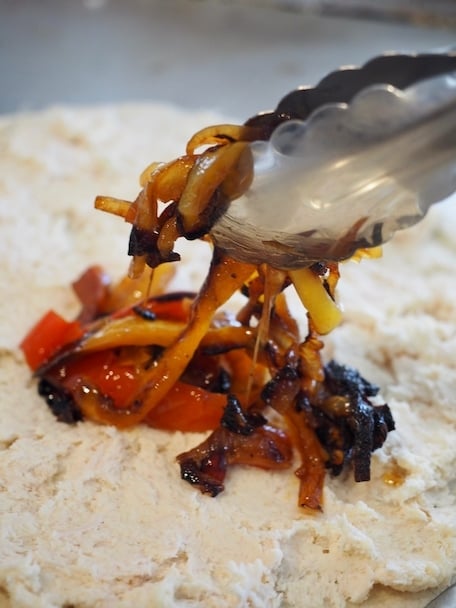 Silver tongs placing caramelized onions and peppers on top of chicken mixture and tortilla | www.thefreshcooky.com