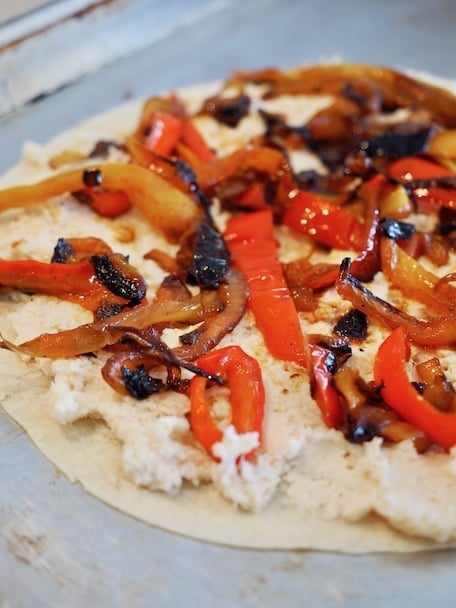 Flour tortilla flat on a baking pan with a layer of chicken and cheese mixture and caramelized onions and peppers on top | www.thefreshcooky.com