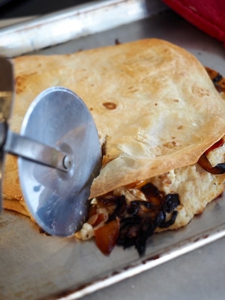 Pizza cutter slicing through quesadilla on baking sheet | www.thefreshcooky.com