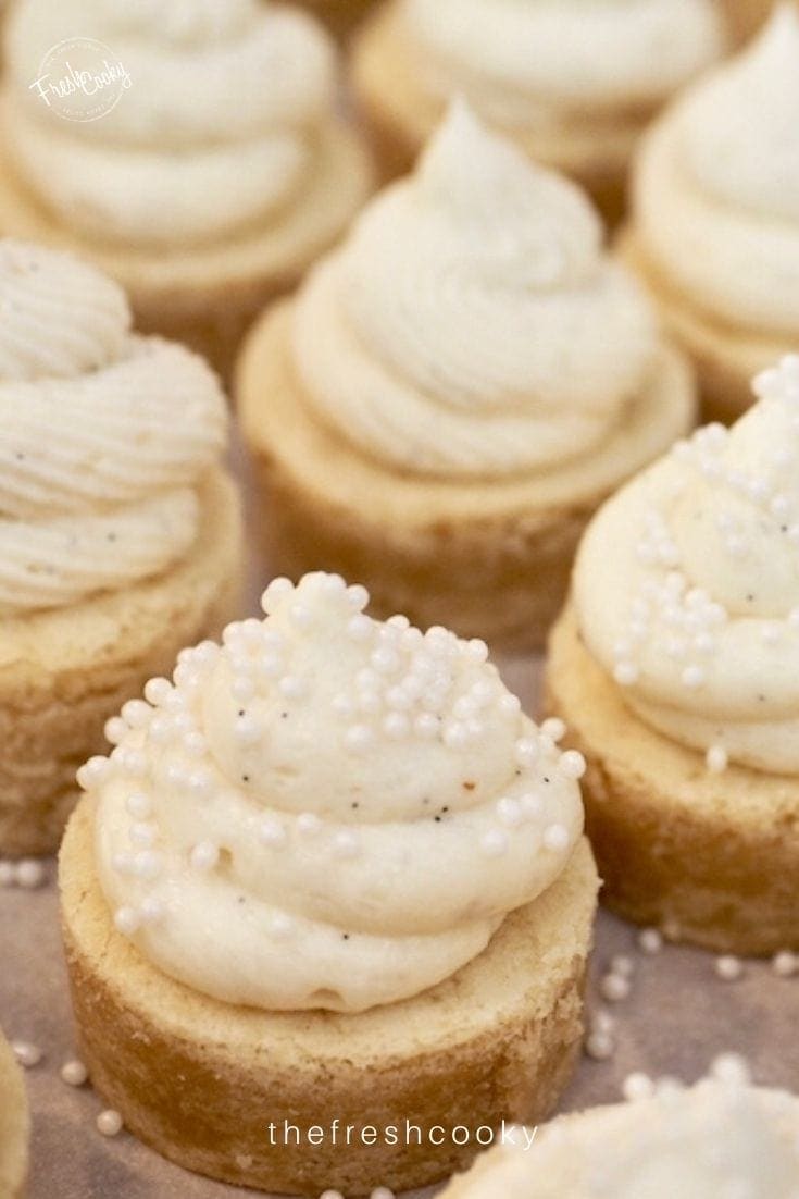 Close up, sugar cookie bite frosted with a swirl of vanilla frosting and decorated with pearl candies.