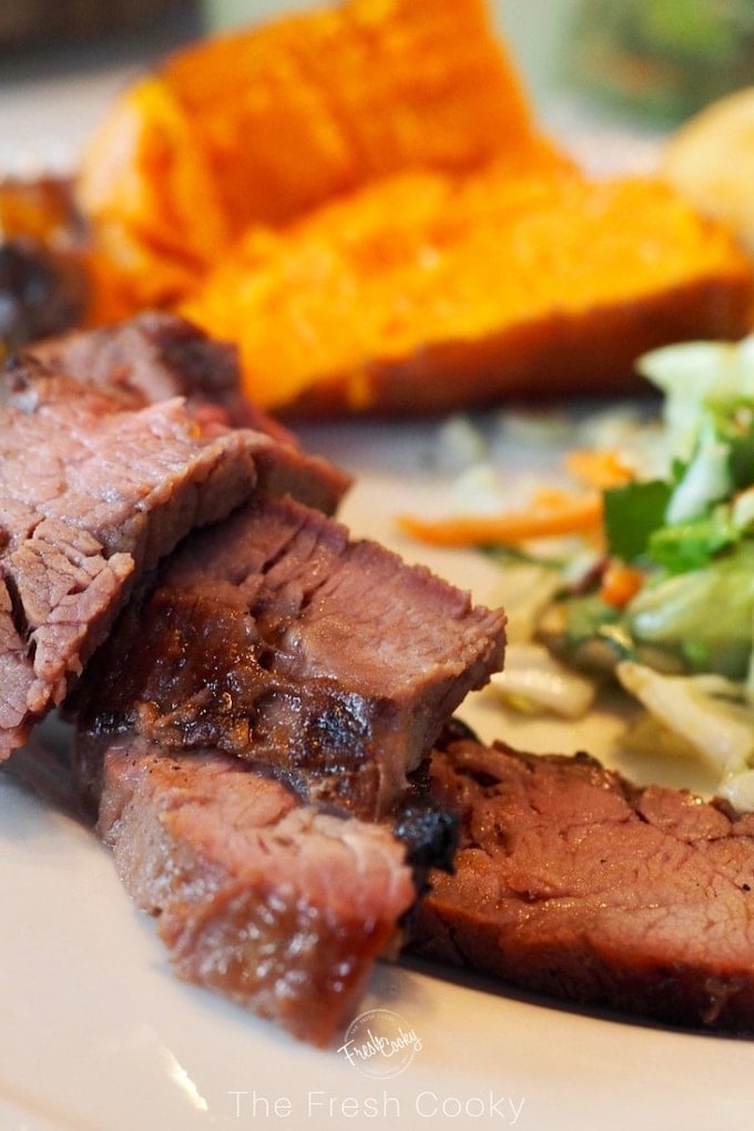 slices of flank steak up close with sweet potato in background and salad on plate.