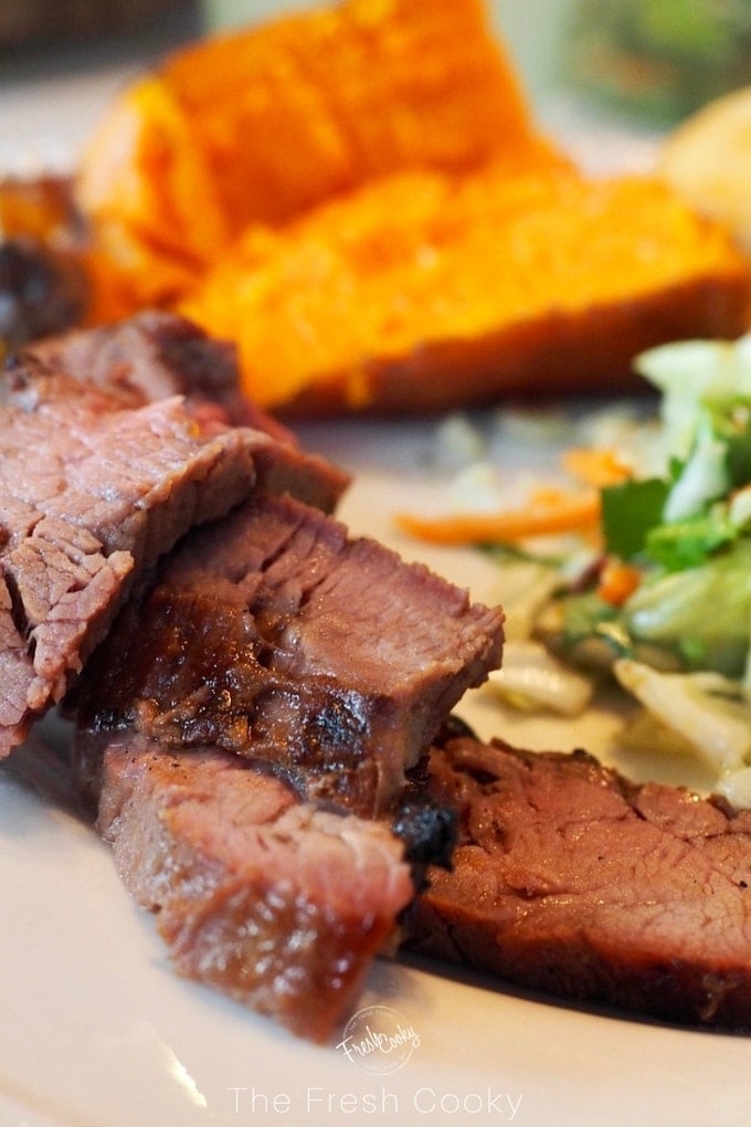 slices of flank steak up close with sweet potato in background and salad on plate. 