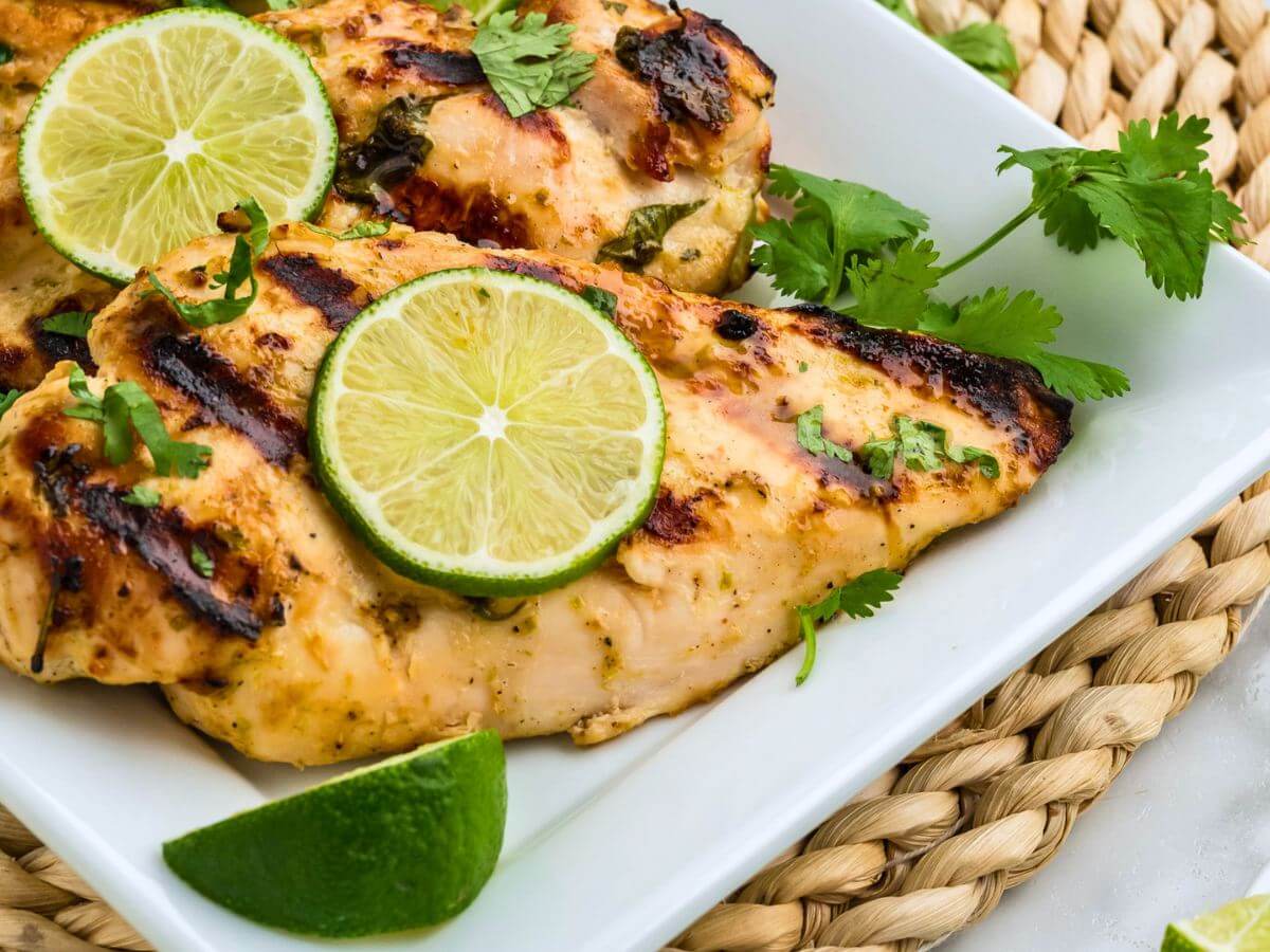 Coconut lime chicken on a square white platter, topped with lime wheels and cilantro.