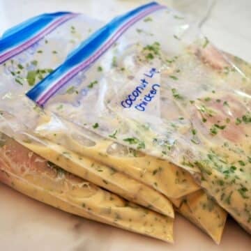 Four freezer baggies with coconut lime chicken and marinade ready for freezer.