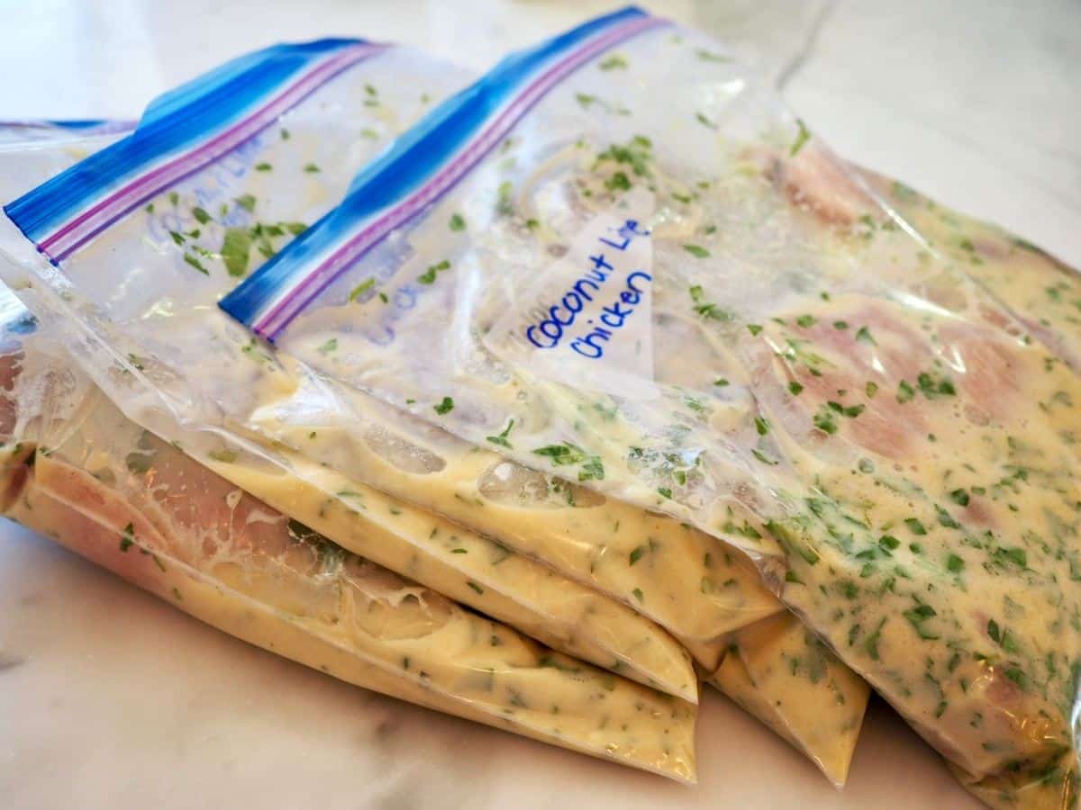 Four freezer baggies with coconut lime chicken and marinade ready for freezer.