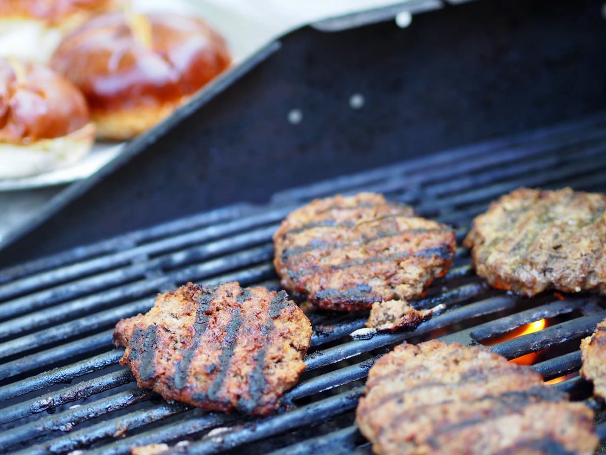 hamburgers on the grill with grill marks, pretzel buns awaiting burgers in background. thefreshcooky.com 