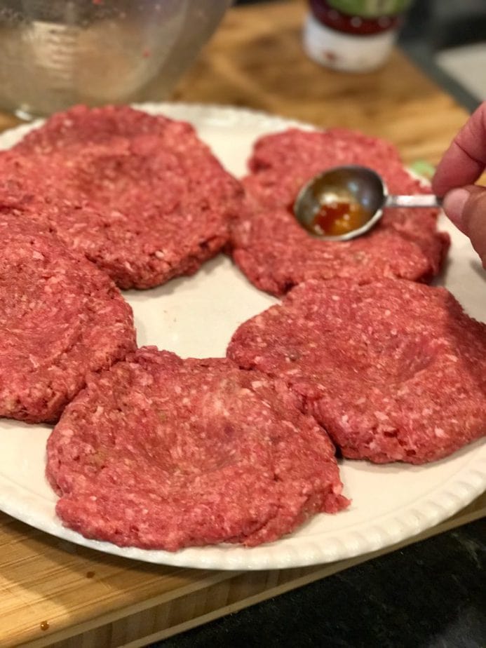 plate of raw hamburger patties using the back of a tablespoon to make a depression in the center or a well to help avoid shrinkage when grilling. thefreshcooky.com