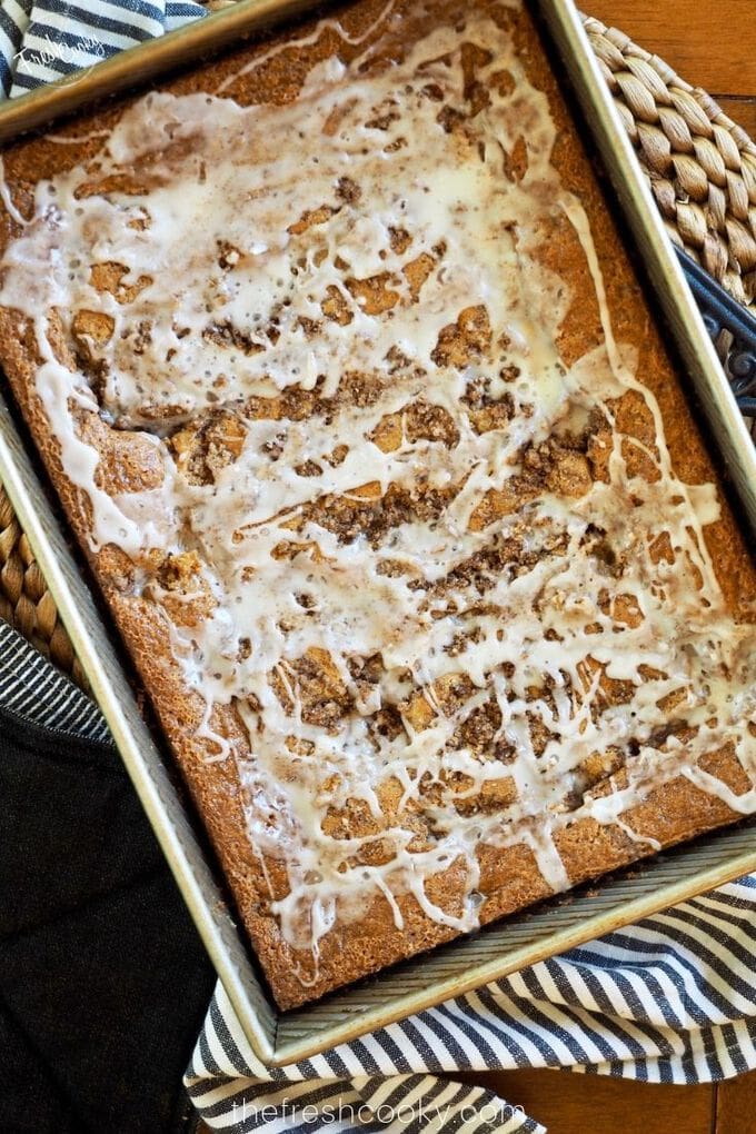 9x13 pan of gluten free coffee cake drizzled with a powdered sugar glaze, laying on a striped towel. Recipe via thefreshcooky.com 