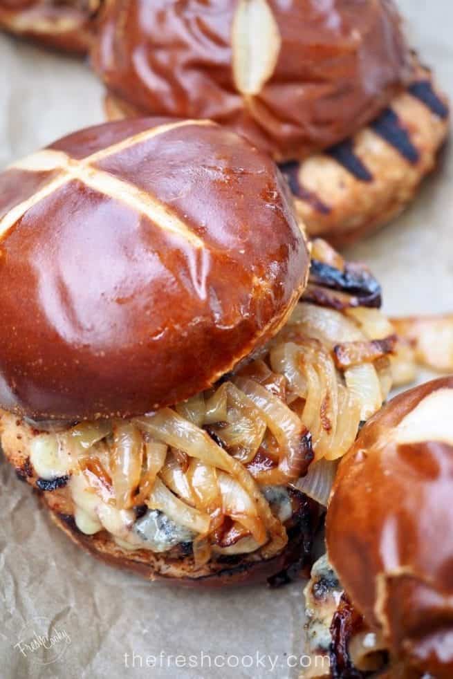 Closeup of turkey burger, grilled with caramelized onions topped with a pretzel roll. thefreshcooky.com