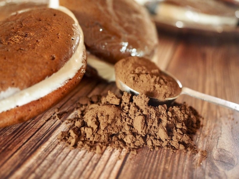 Image of Classic New England Whoopie Pies on wood table with spoonful of cocoa.