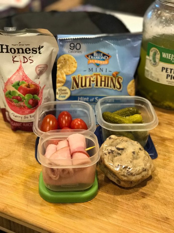 school lunch. Honest Kids cherry fruit punch pouch, mini nut things, petite dill pickles in jar, and some in small plastic container, grape tomatoes and rolled ham with toothpick in small rubbermaid. Two chocolate chip cookies, frozen and in plastic wrap. 