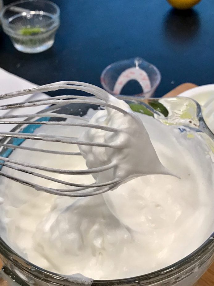 Whisk beater with fluffy egg whites whipped and puffy in a glass m ixing bowl