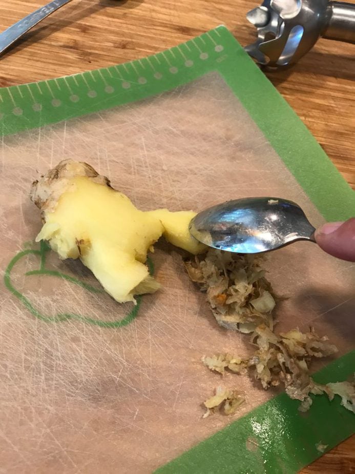 Using a spoon to scrape the ginger skin off of fresh ginger. 