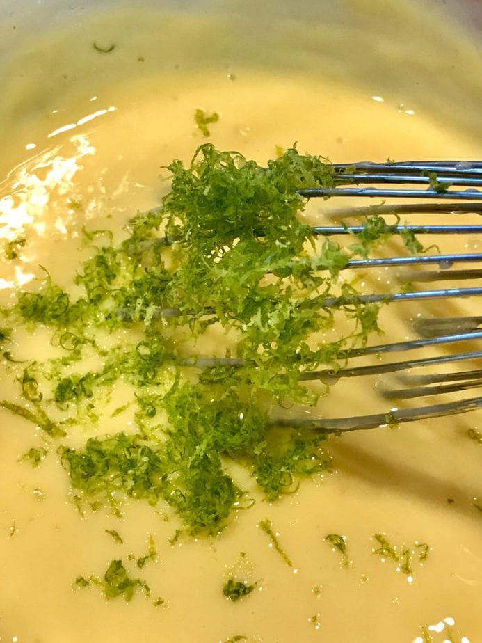 Key lime torte filling closeup with lime zest on top and wire whisk. 