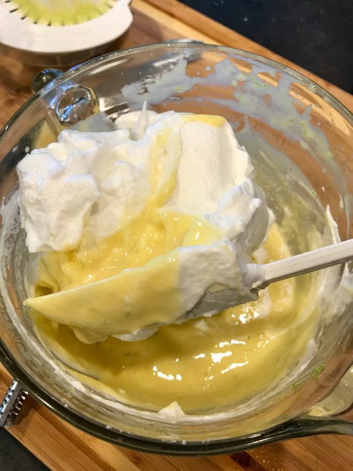 Key lime mixture in glass mixing bowl with large spatula folding or turning whipped egg whites into the batter.